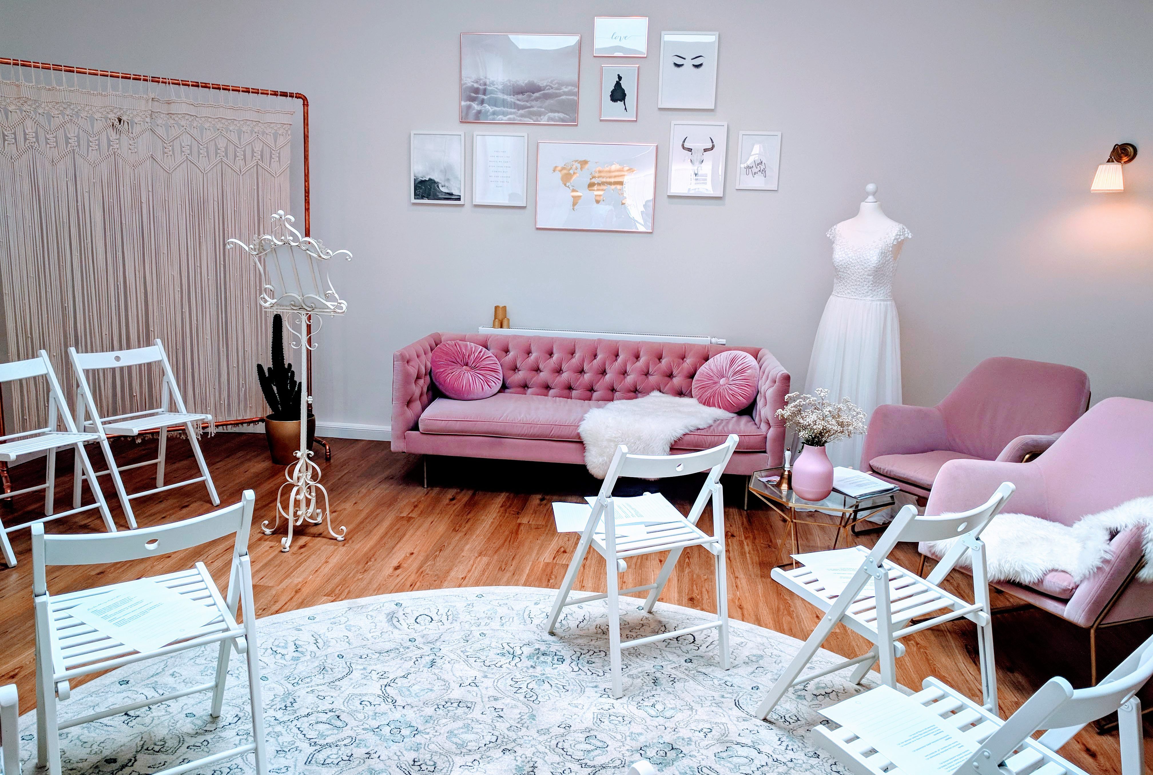 Das Bild zeigt den Showroom des "Das Brautstübchen" in Remscheid. In der Mitte des Raums stehen weiße Klappstühle, ausgerichtet zu einem Vintage-Trauständer im vorderen Bereich.